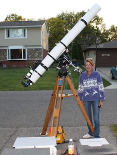 a woman standing in front of a telescope on top of a tripod near a house