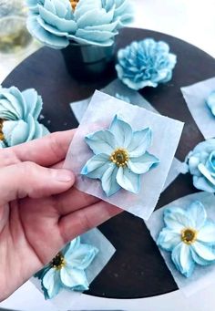 someone is holding some paper flowers on top of a cake