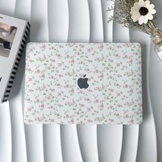 an apple laptop computer sitting on top of a white table next to a vase with flowers