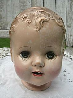 an old doll head sitting on top of a white tablecloth with a wooden fence in the background