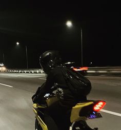 a man riding on the back of a yellow motorcycle down a street at night time