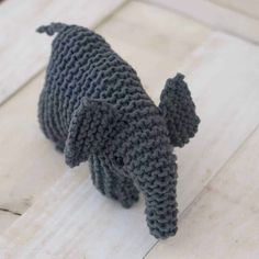 a gray knitted elephant toy sitting on top of a white wooden floor next to a window