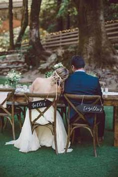 a bride and groom sitting at a wooden table with their names on the back of them