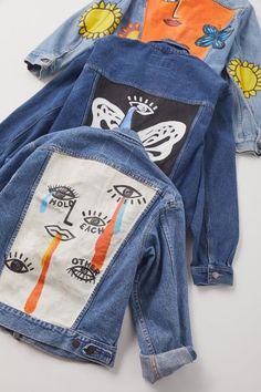 two jean jackets with designs on them sitting next to each other