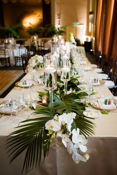 a long table with white flowers and greenery on it is set for a formal dinner