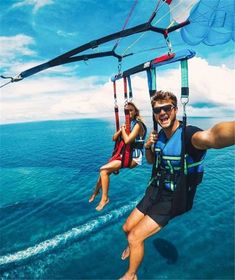 two people riding on the back of a boat while holding onto parachutes in the air