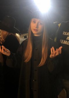 a woman standing in front of a camera holding her hands out to the side while wearing a hat