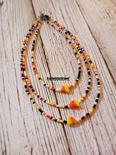 three necklaces with orange, yellow and black beads on a wooden background that says halloween's