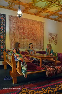 two women sitting on a couch in front of a wall hanging with tapes and rugs