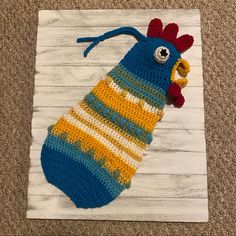 a crocheted blue and yellow chicken on a white wooden board with wood planks