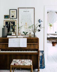 a piano in a living room next to a table with flowers and pictures on it