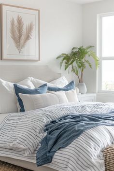 a white bed with blue and white striped comforter in a bedroom next to a potted plant