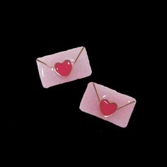 pair of pink and gold earrings with red heart in the shape of envelopes on black background