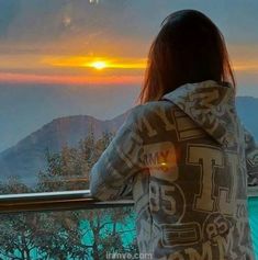 a woman looking out at the mountains from a balcony with a sunset in the background