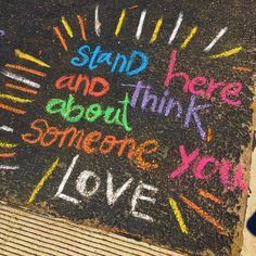 chalk writing on the ground with words written in different languages and colors, along with someone holding a cell phone