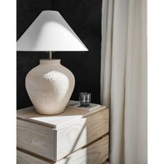 a white vase sitting on top of a wooden table next to a lamp with a white shade