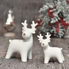 two white ceramic reindeer figurines sitting on a wooden table next to a christmas tree