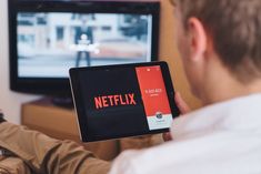 a man sitting in front of a tv holding an ipad with the netflix logo on it