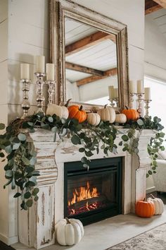 a fireplace with candles, pumpkins and greenery on it in front of a mirror