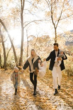 a man and woman holding hands as they walk down a leaf covered path with their baby