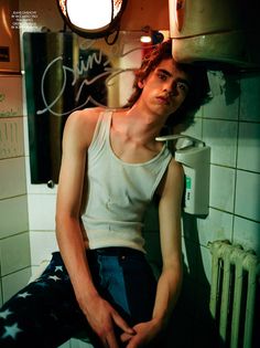 a young man sitting on top of a toilet in a bathroom next to a radiator