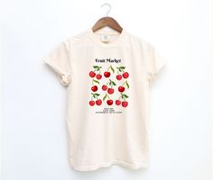 Celebrate the vibrant charm of a local fruit market with our "Fruit Market" Event T-Shirt. Featuring a delightful illustration of cherries, this design includes the event details above and below the artwork. The text reads "Fruit Market" above and "02 July, 2024 | 8:30am - 3:00pm | 123 Anywhere St., Any City, ST 12345" below. Crafted from high-quality 100% ring-spun US cotton, this Comfort Colors 1717 tee offers a relaxed fit perfect for casual and semi-formal settings. The medium-weight fabric ensures long-lasting comfort and durability, while the garment-dyed finish provides a soft, vintage look and feel. Pre-shrunk for a consistently great fit, this t-shirt is ideal for anyone looking to commemorate a special event or simply enjoy a stylish, comfortable tee. Key Features: -100% Ring-Spu Organic Graphic Print Top For Spring, Organic Tops With Graphic Print For Spring, Organic Graphic Print T-shirt For Spring, Organic Short Sleeve T-shirt For Spring, Organic White T-shirt For Summer, Graphic Tee With Fruit Design For Spring, Spring Organic White T-shirt, Spring Fruit Print Graphic Tee Shirt, Spring Fruit Print Graphic Tee