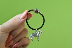 a woman holding onto a black cord bracelet with a silver dog charm on it's end