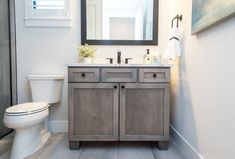 a white toilet sitting next to a wooden sink vanity in a bathroom under a mirror