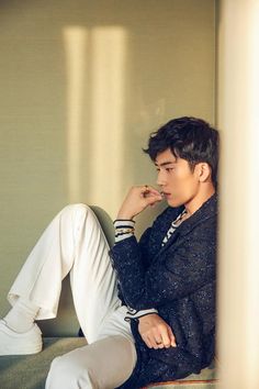 a young man sitting on top of a couch next to a white wall with his hand under his chin