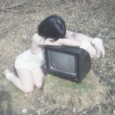 a young woman sitting on the ground next to a small tv in front of her