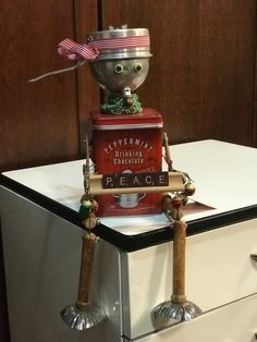 a toy robot is sitting on top of a refrigerator and holding a sign that says peace