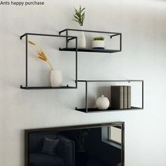 three black shelves with plants and vases on them against a white wall in a living room