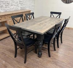 a wooden table with black chairs in front of a white brick wall and wood flooring