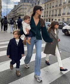 a woman and two children walking across a crosswalk in the middle of a city