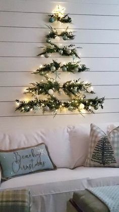 a christmas tree is hanging on the wall above a white couch with plaid throw pillows