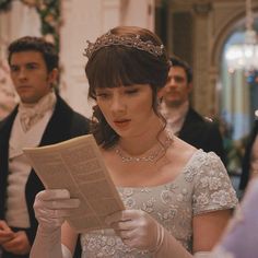 a woman wearing a tiara reading a newspaper in front of other men and women