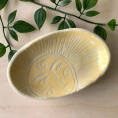 a yellow bowl sitting on top of a table next to some green leafy branches