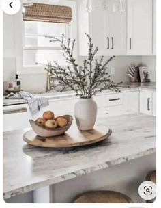 a bowl of fruit sitting on top of a kitchen counter next to a vase filled with flowers