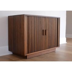 a wooden cabinet sitting on top of a hard wood floor next to a white wall