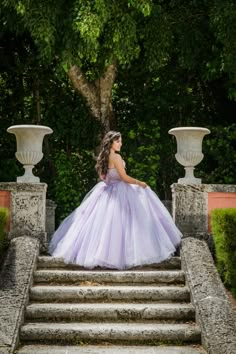 a woman in a ball gown standing on some steps with trees and bushes behind her