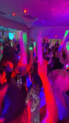 a group of people dancing in a room with purple and green lights on the ceiling