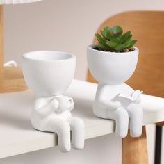 two white ceramic figures sitting on top of a table next to a potted plant