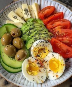 an egg, avocado, tomato and olives on a plate