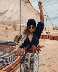 a woman standing on top of a sandy beach next to a tarp covered tent