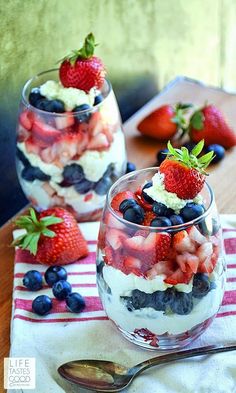 two glasses filled with fruit sitting on top of a table next to strawberries and blueberries