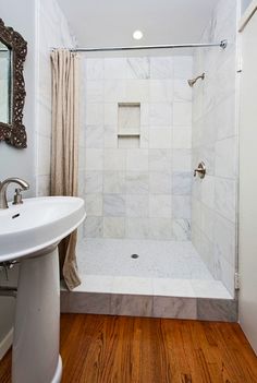 a bathroom with a shower, sink and mirror on the wall next to wood flooring