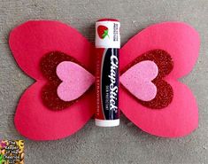 a pink and red butterfly with glitter on it's wings next to a tube of glue