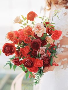 a bride holding a bouquet of red and pink flowers