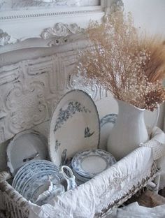 a basket filled with dishes and flowers in front of a white dresser topped with plates