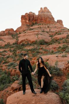 a man and woman standing on top of a rock in front of some red rocks